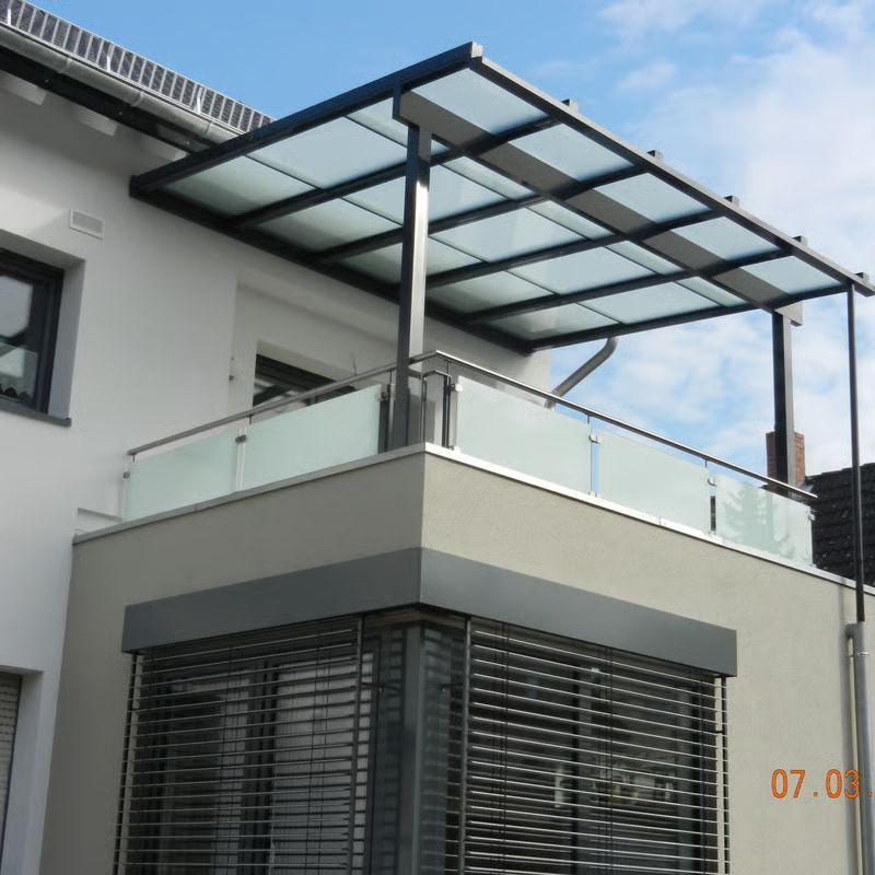 Moderner Hausbalkon mit Glasgeländer und schwarzem Metall-Glas-Vordach über einer weißen Fassade