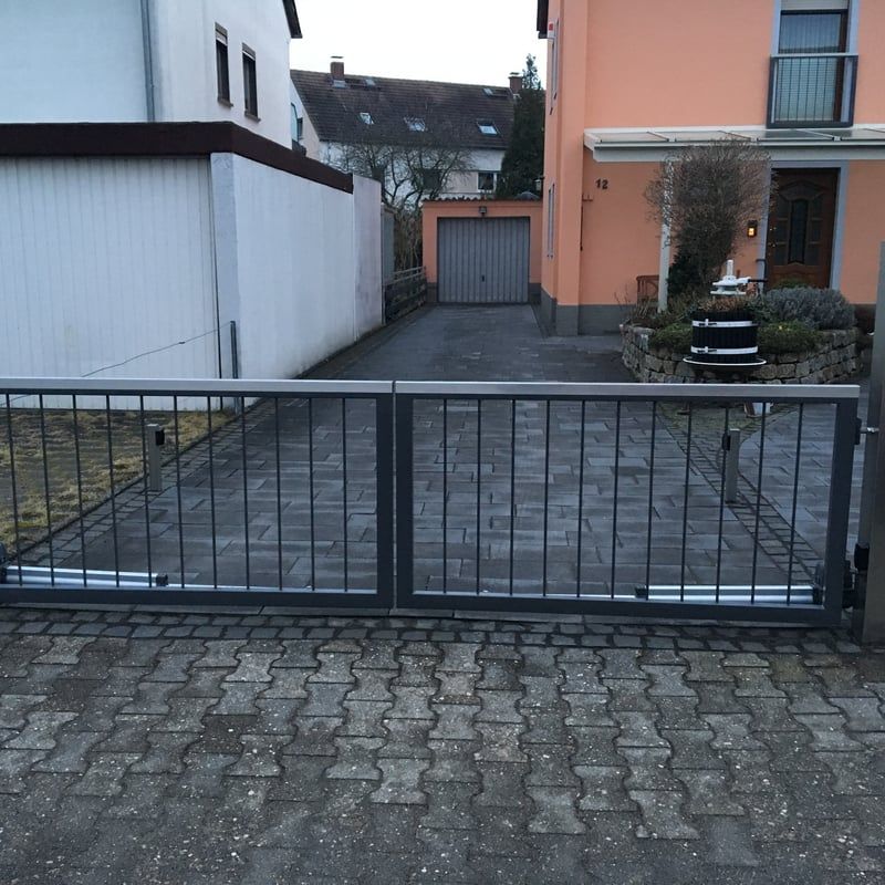 Wohnzufahrt mit einem geschlossenen schwarzen Metalltor zwischen den Häusern, von der Straße aus gesehen.