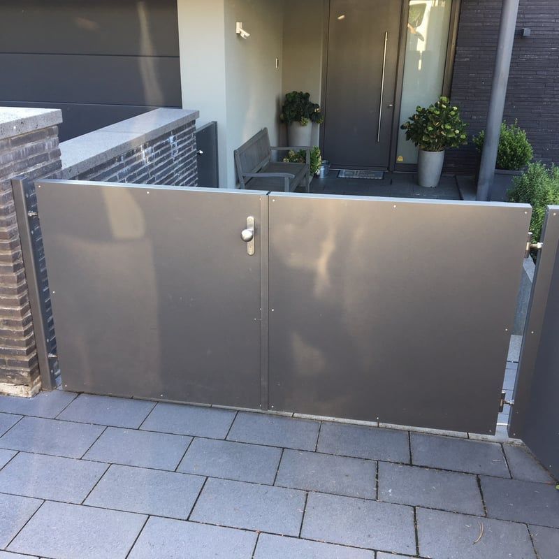 Eingangstor eines modernen Hauses mit grauen Paneelen, Topfpflanzen und gefliesten Stufen.