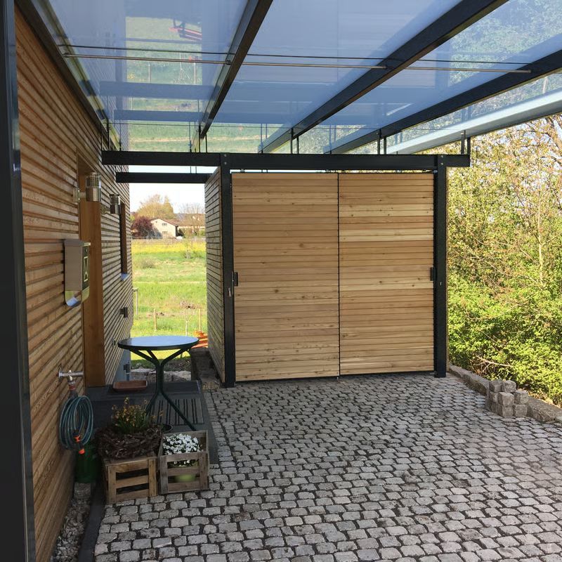Überdachte Terrasse mit Kopfsteinpflasterboden, Holzschuppen und Gartenblick unter einem Glasdach