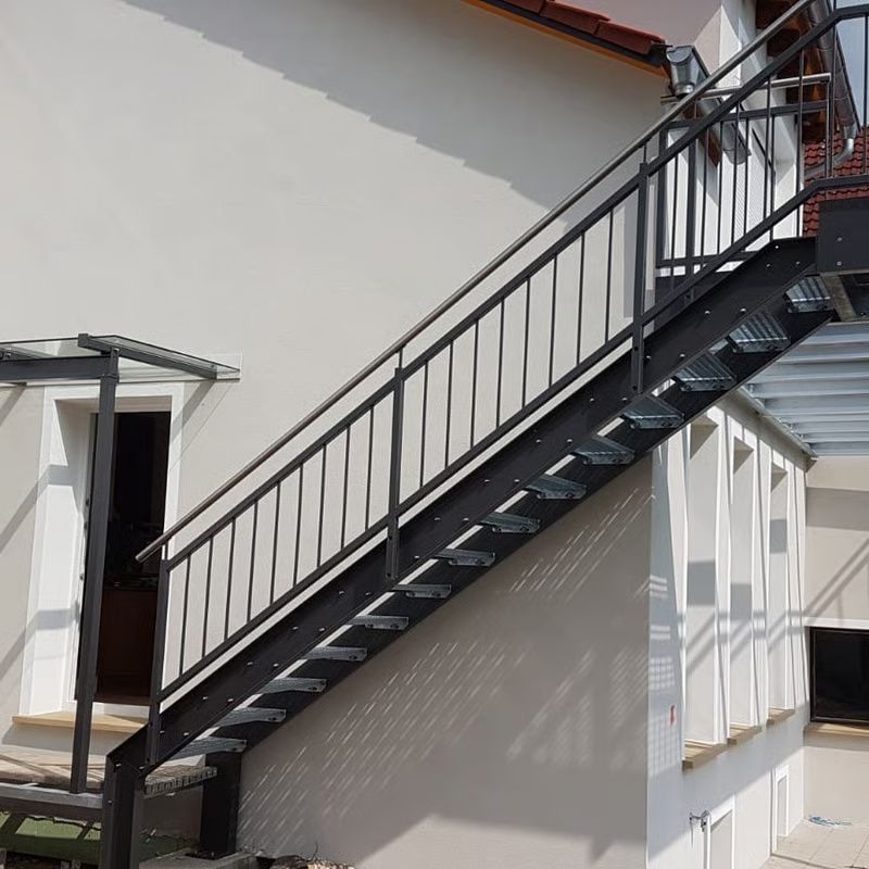 Schwarze Metalltreppe mit Geländer, die an einer weißen Gebäudefassade befestigt ist