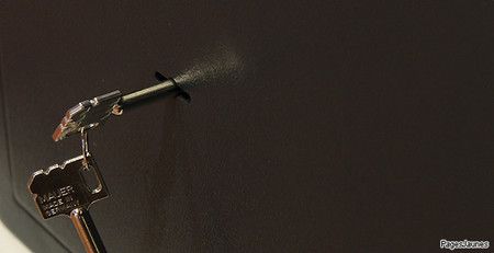 Une seringue pulvérise un brouillard, maintenue par une clé, sur un fond sombre.