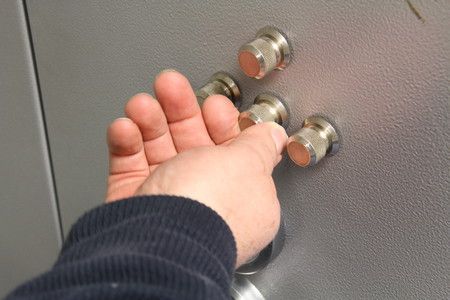 Manipulation manuelle d'un bouton argenté sur un panneau gris comportant quatre autres boutons similaires.