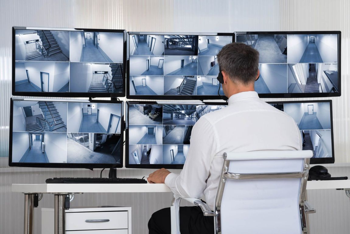 Un homme, assis à son bureau, surveille les flux vidéo des caméras de sécurité sur plusieurs écrans.