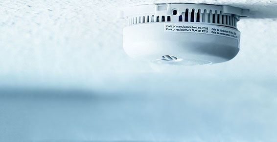 Détecteur de fumée blanc fixé au plafond blanc.