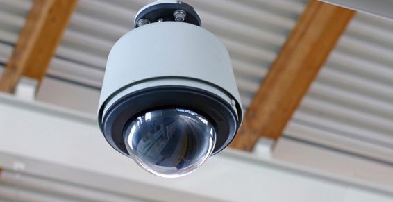 Caméra de sécurité fixée sur un plafond blanc et marron.