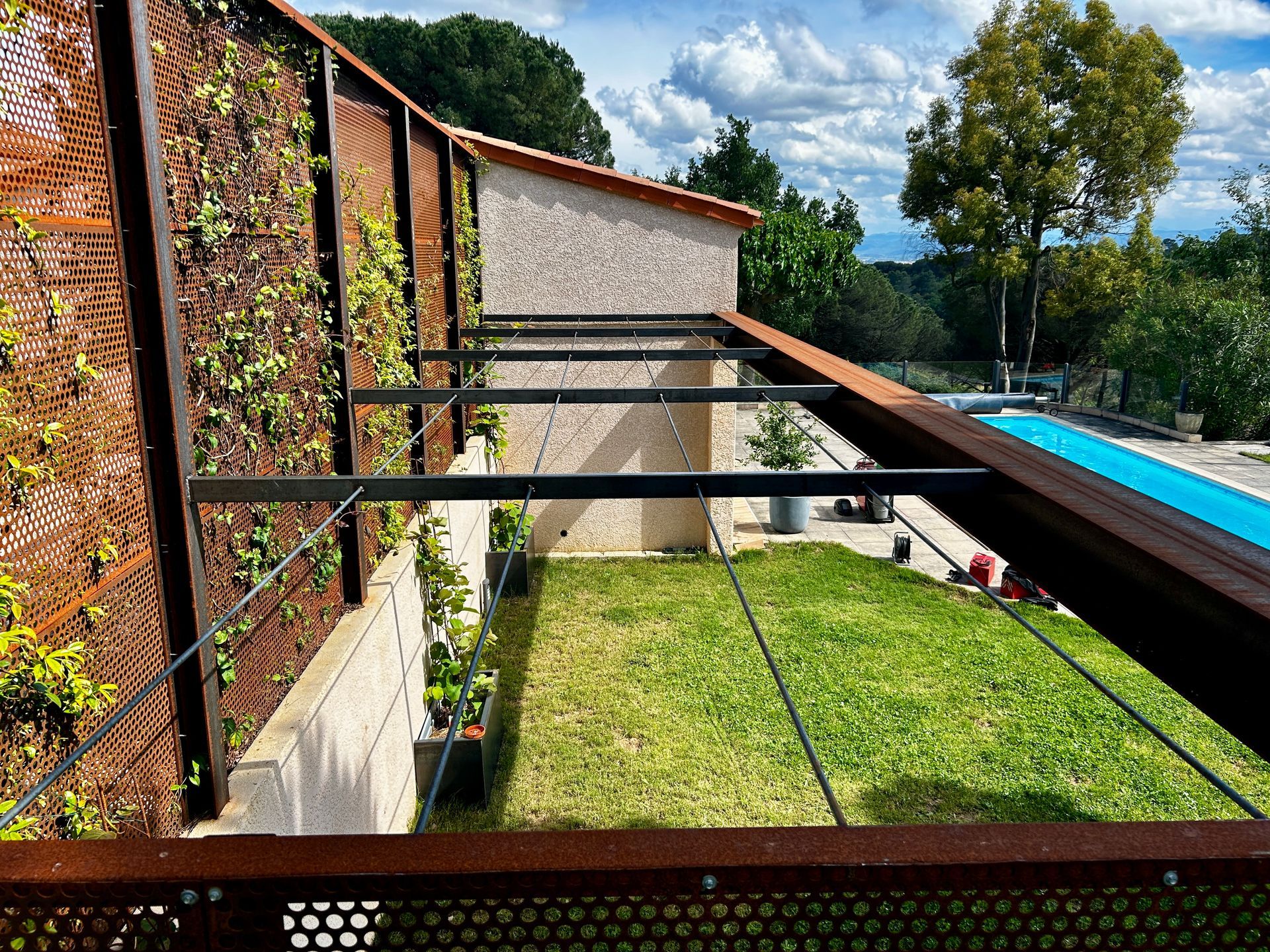 Pergola rouillée au-dessus d'une terrasse avec table et chaises près d'une piscine.