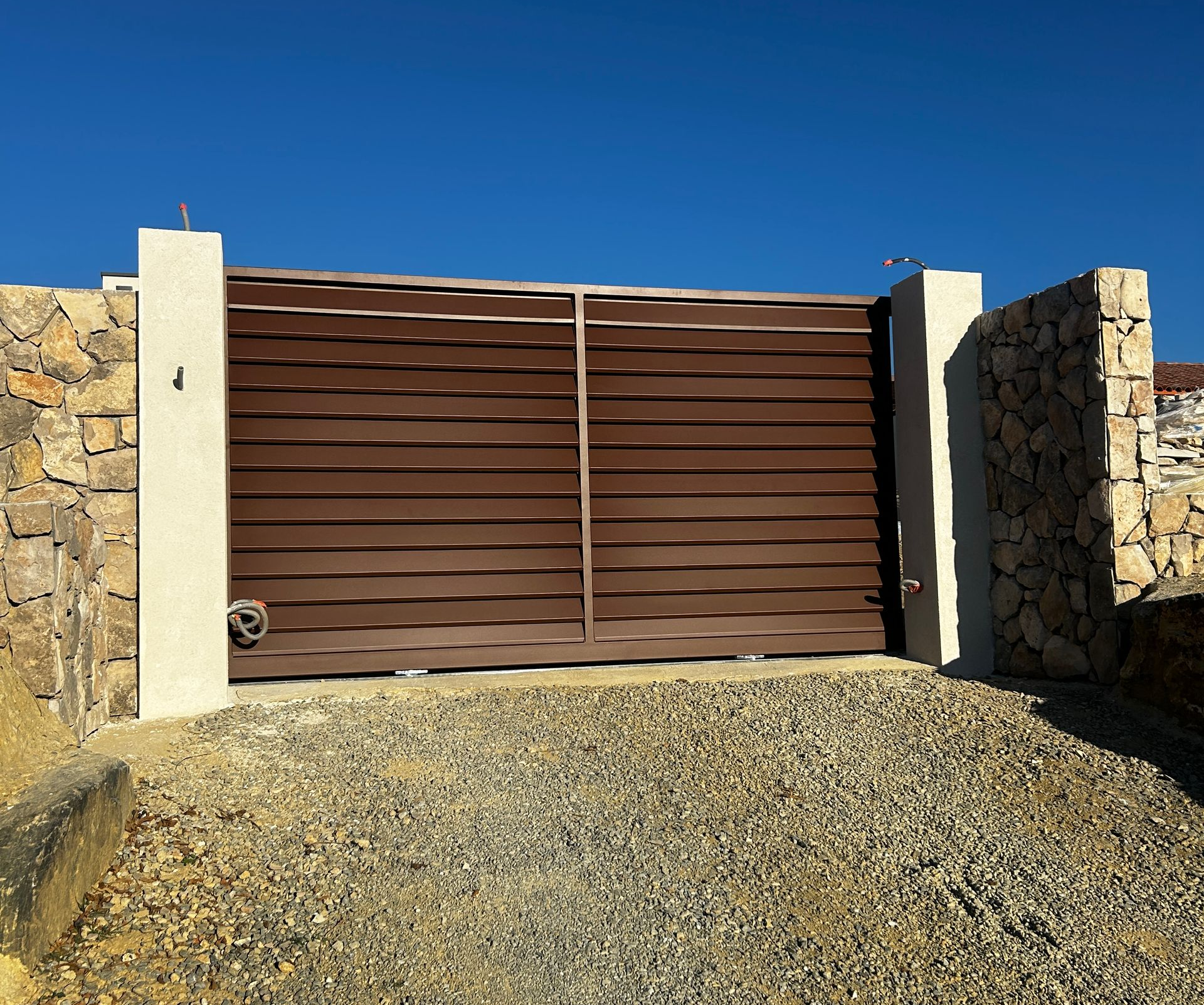 Portail en métal effet rouillé à lattes horizontales style persienne, entre deux piliers en béton beige.