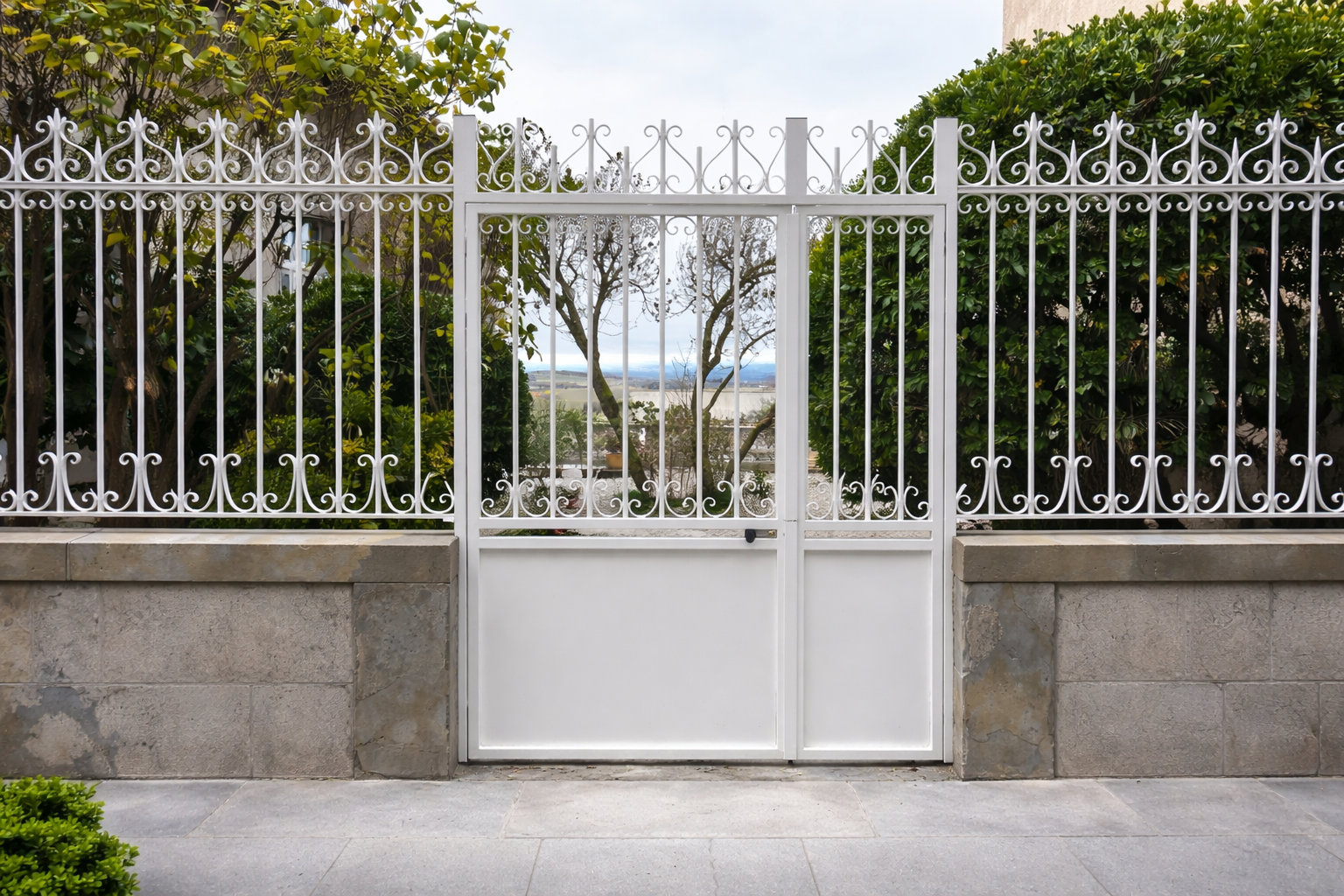 Portail et clôture en métal blanc. Le portail possède une partie inférieure pleine et une partie supérieure décorative.