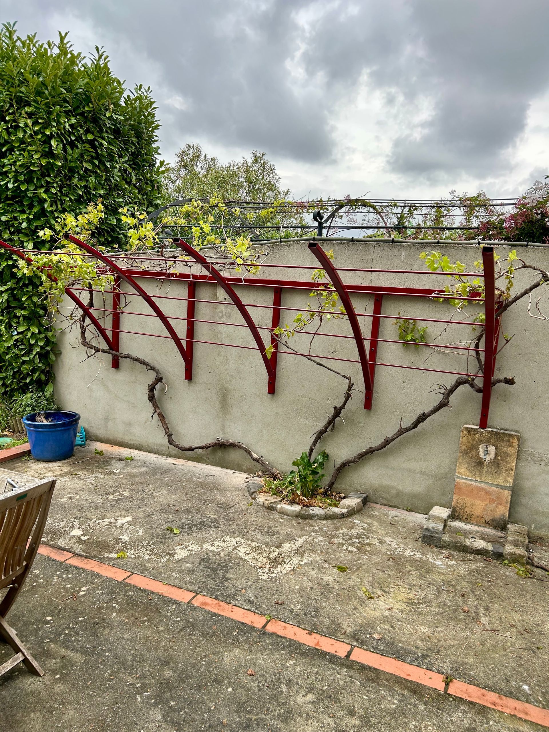 Treille métallique rouge dans terrasse avec plantes grimpantes.