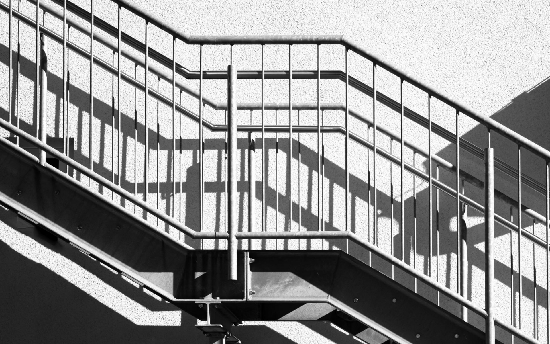 Un escalier en métal se détache sur un mur blanc. Garde corps en noir et blanc.