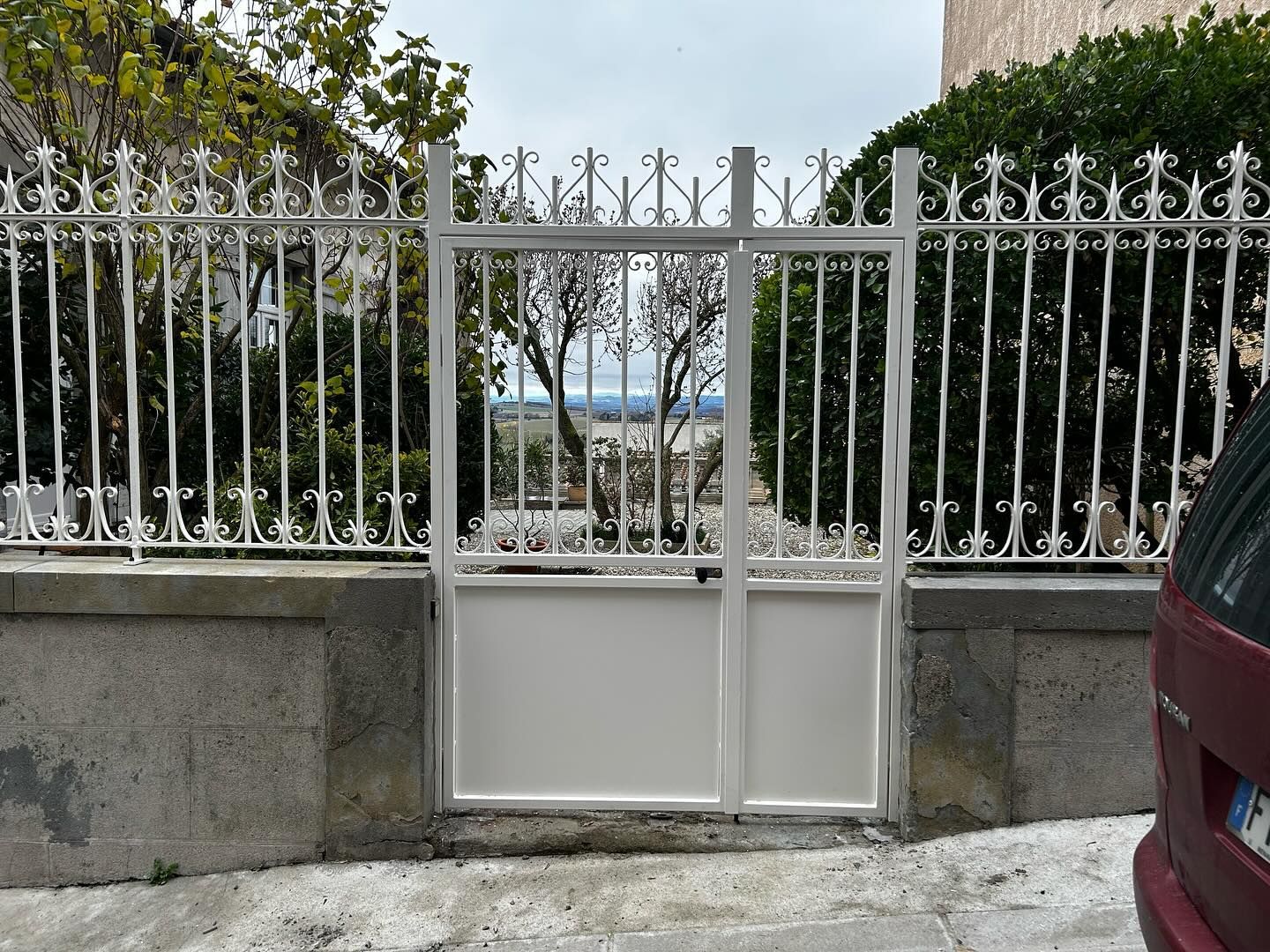 Portail et clôture en métal blanc. Le portail possède une partie inférieure pleine et une partie supérieure décorative.