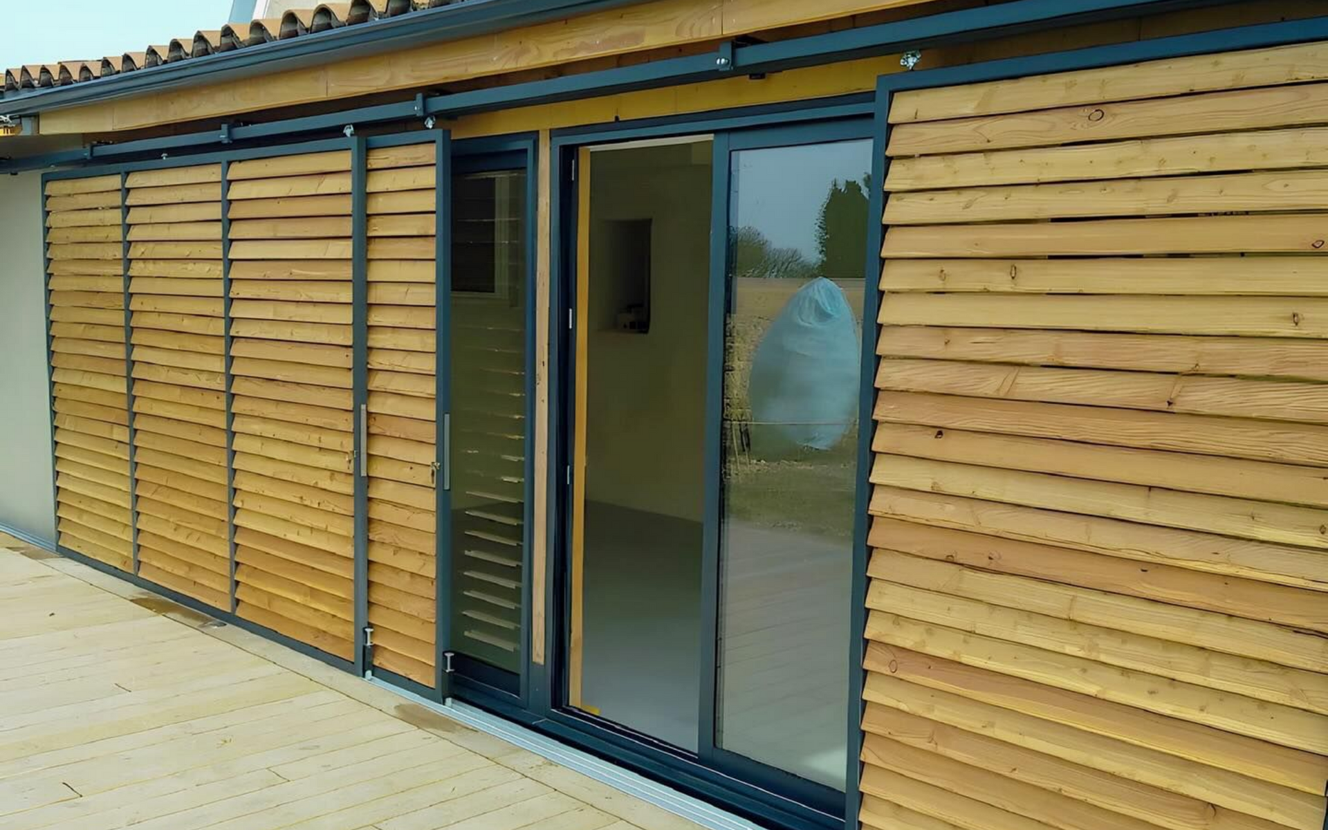 Extérieur d'un bâtiment avec bardage en bois et portes coulissantes ; les lattes de bois sont réglables.