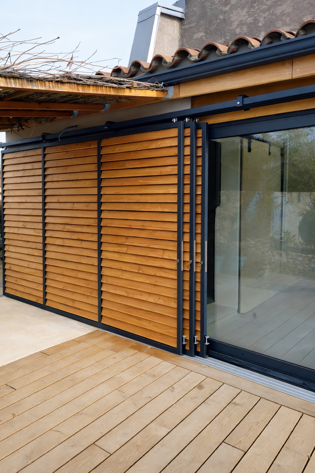 Extérieur d'un bâtiment avec bardage en bois, portes coulissantes en verre et revêtement en lattes de bois.