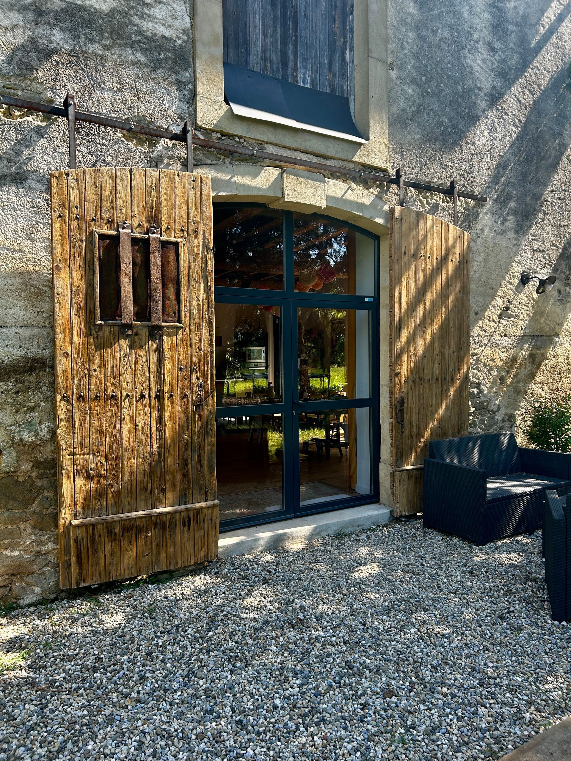 Vue extérieure d'un bâtiment avec des volets en bois et des portes coulissantes en verre, sur une terrasse en bois.