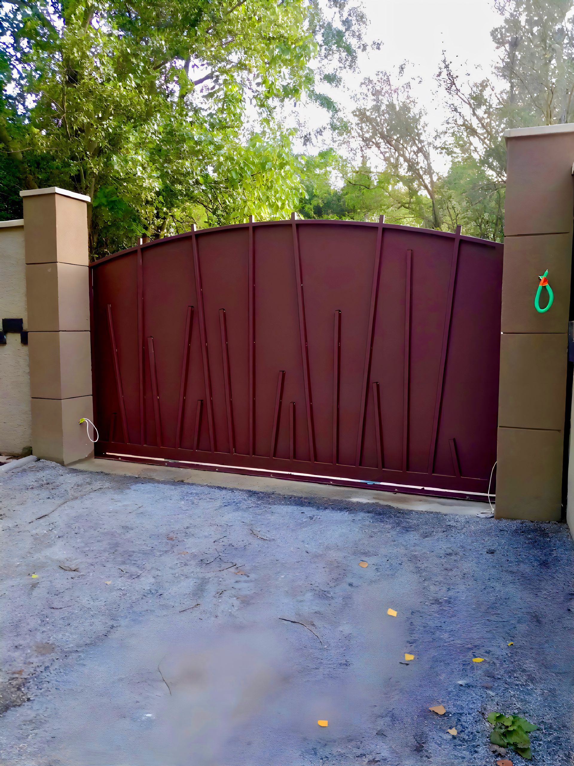 Un portail en métal effet rouillé artistique, encadré de piliers de pierre.