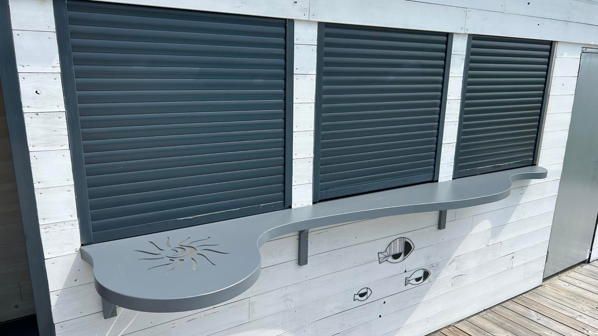 Bâtiment blanc avec trois fenêtres à volets gris et un comptoir assorti en saillie.