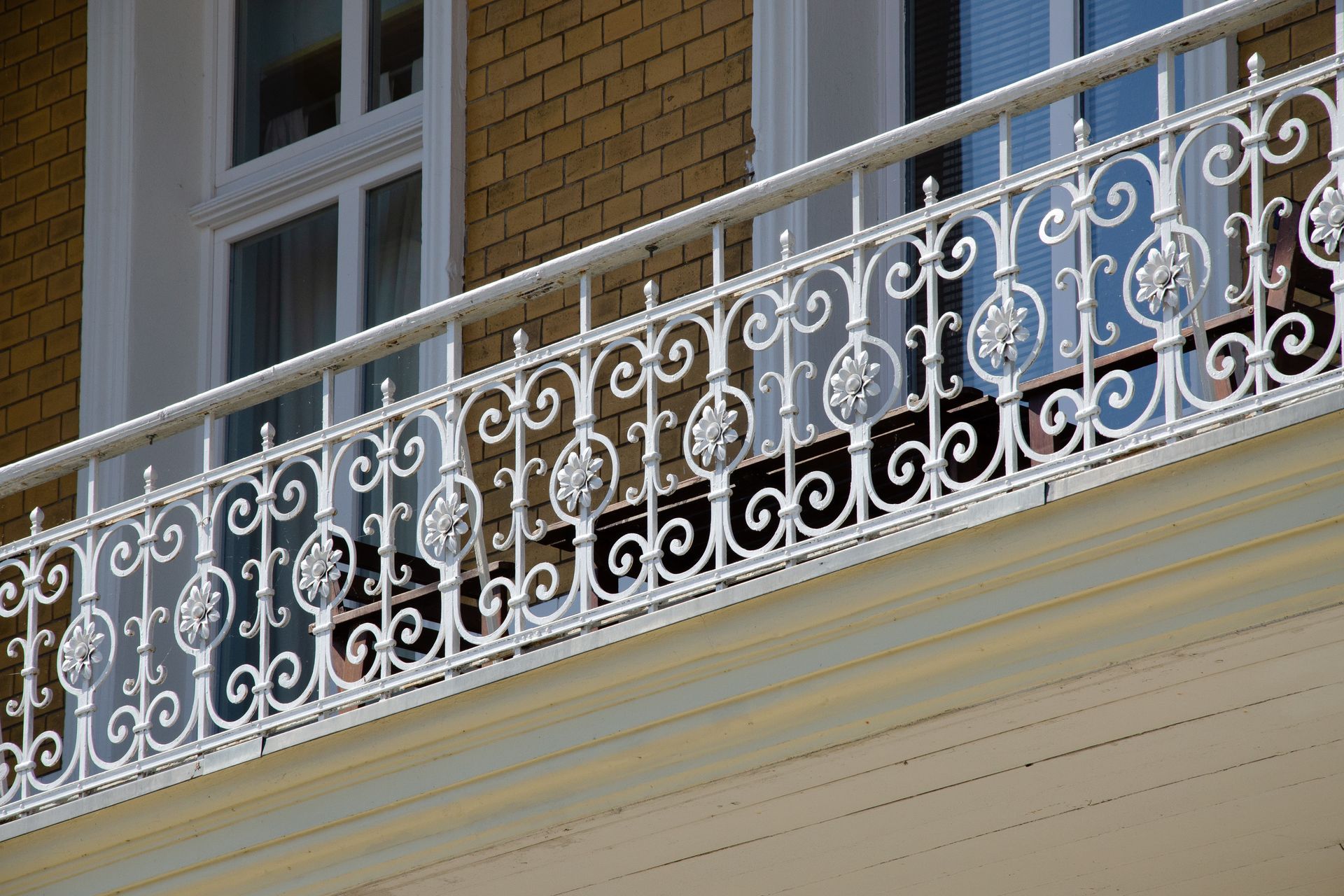 Bâtiment beige de deux étages avec balcon, garde corps en fer forgé blanc.
