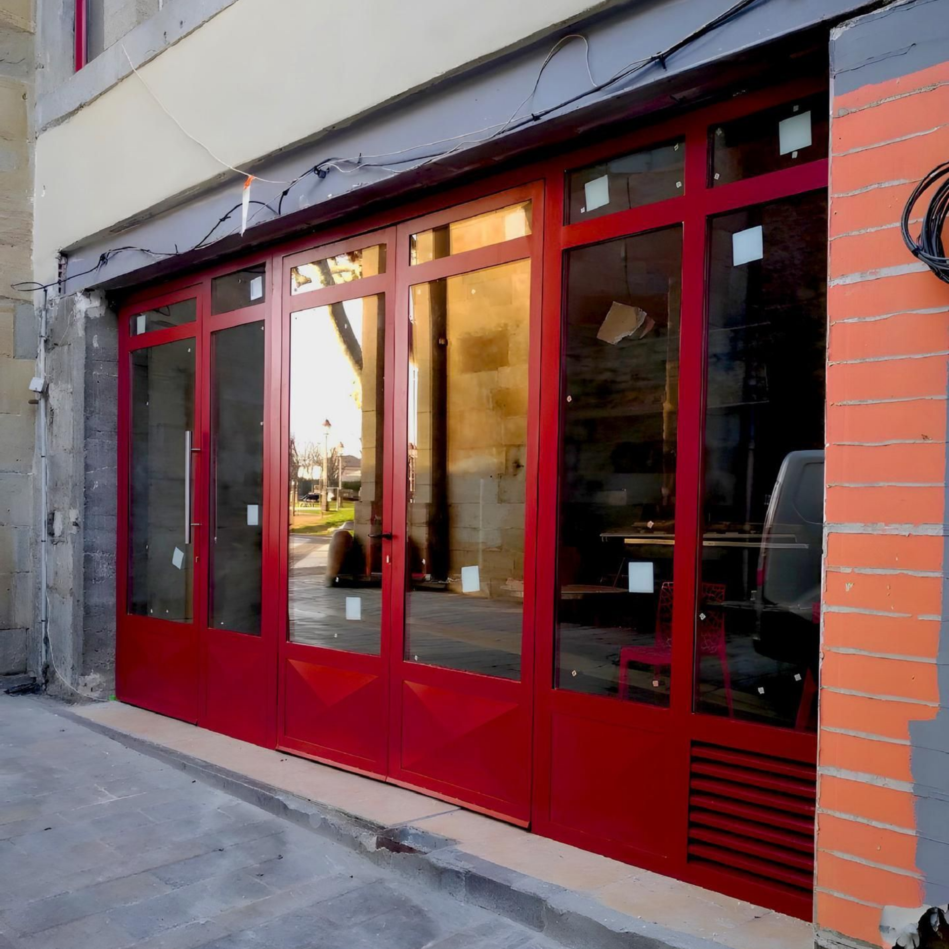 Portes et fenêtres vitrées à cadre rouge d'un magasin, dans une rue, reflétant l'extérieur.