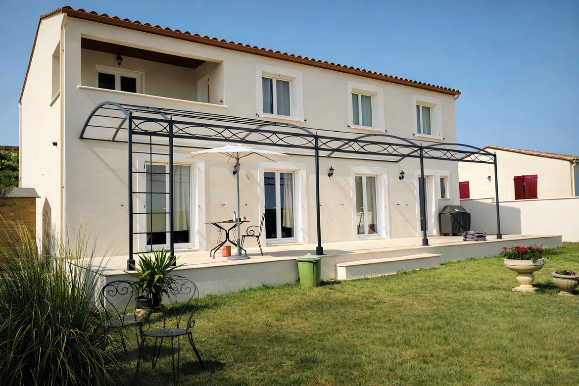 Maison à deux étages avec volets bleus, une pergola et un jardin gazonné sous un ciel bleu.