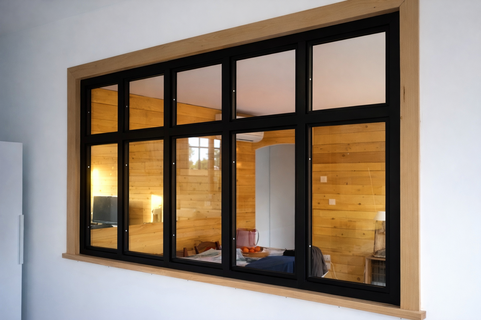 Fenêtre à plusieurs carreaux à cadre noir reflétant un intérieur en bois ; moulures beiges au mur.