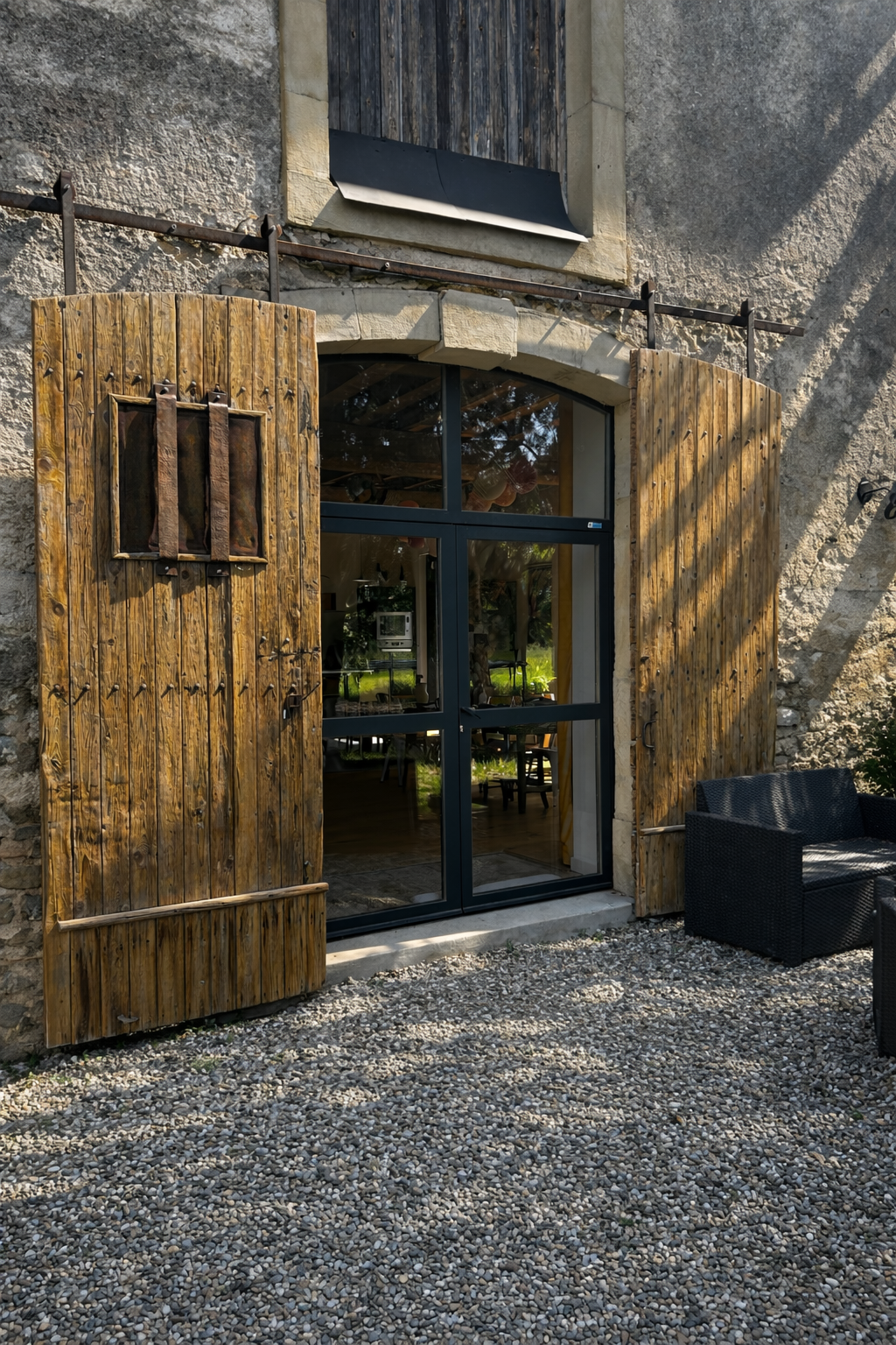 Vue extérieure d'un bâtiment avec des volets en bois et des portes coulissantes en verre, sur une terrasse en bois.