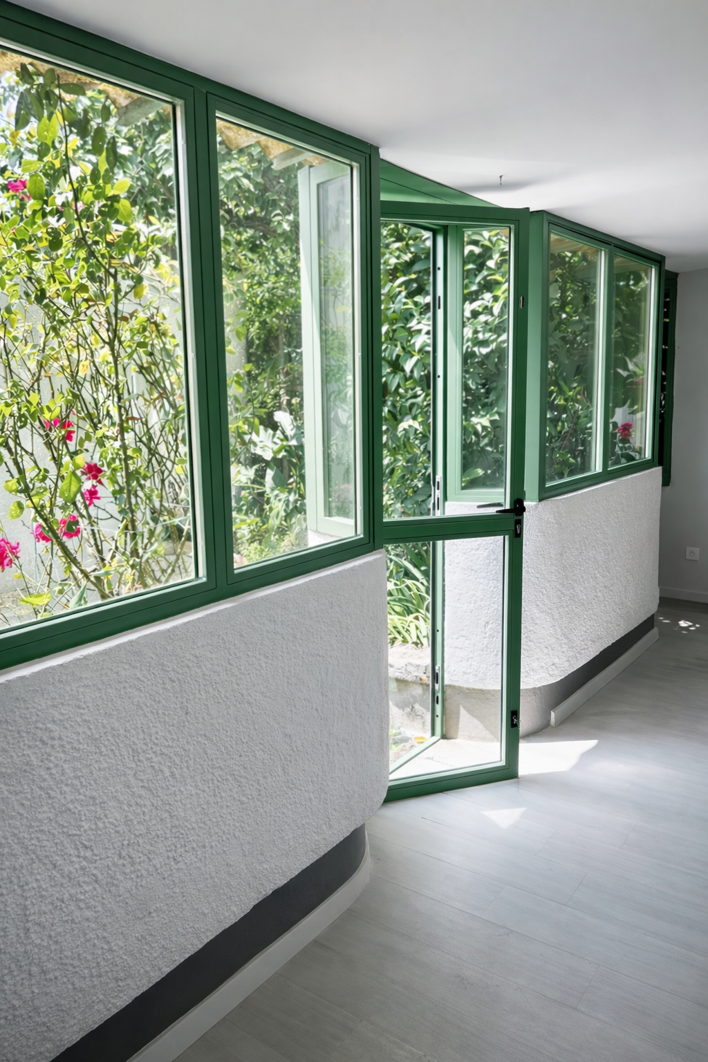 Verrière en acier verte avec porte dans véranda et vue sur jardin.