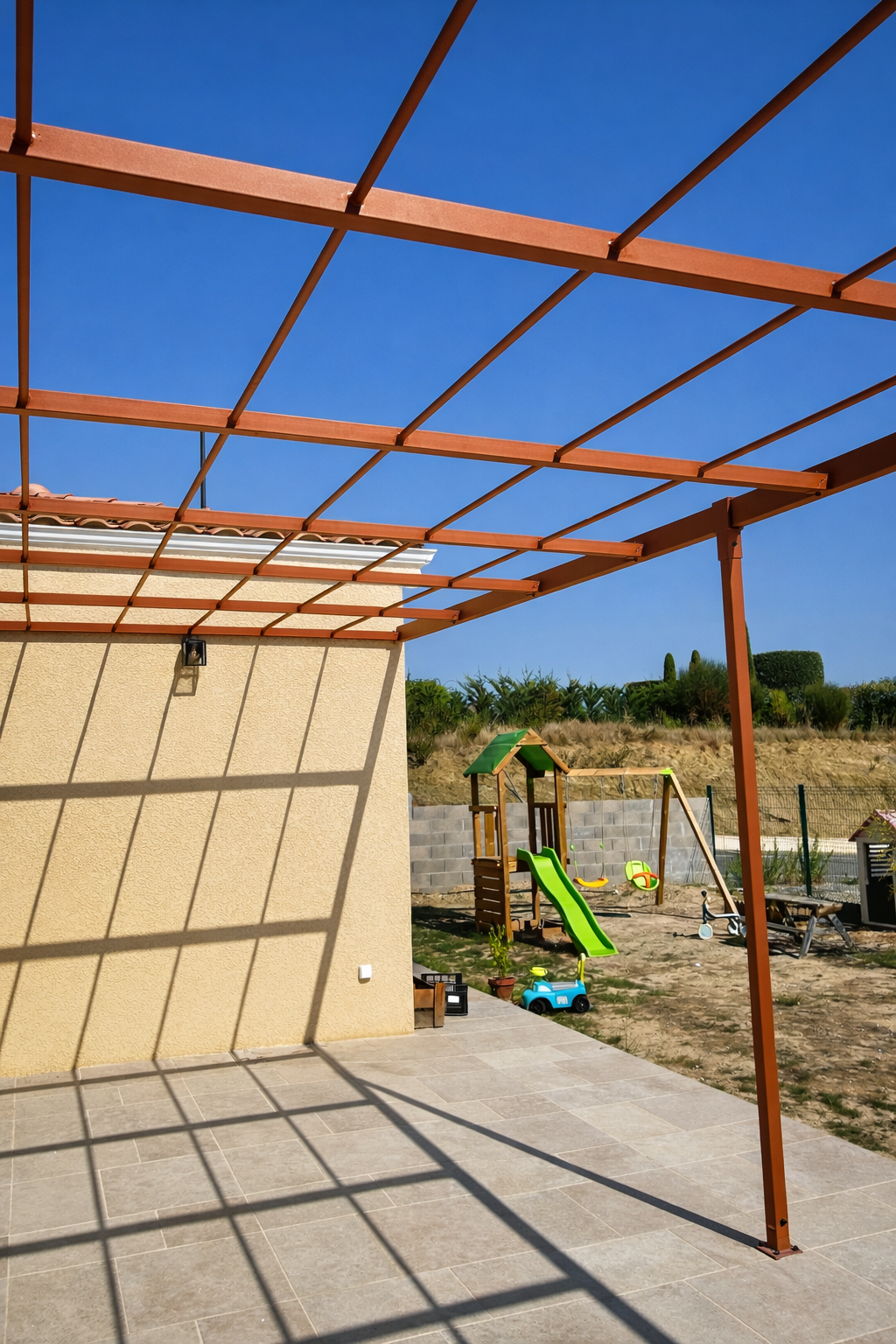 Maison beige avec terasse, une pergola effet rouillé et un ciel bleu clair.