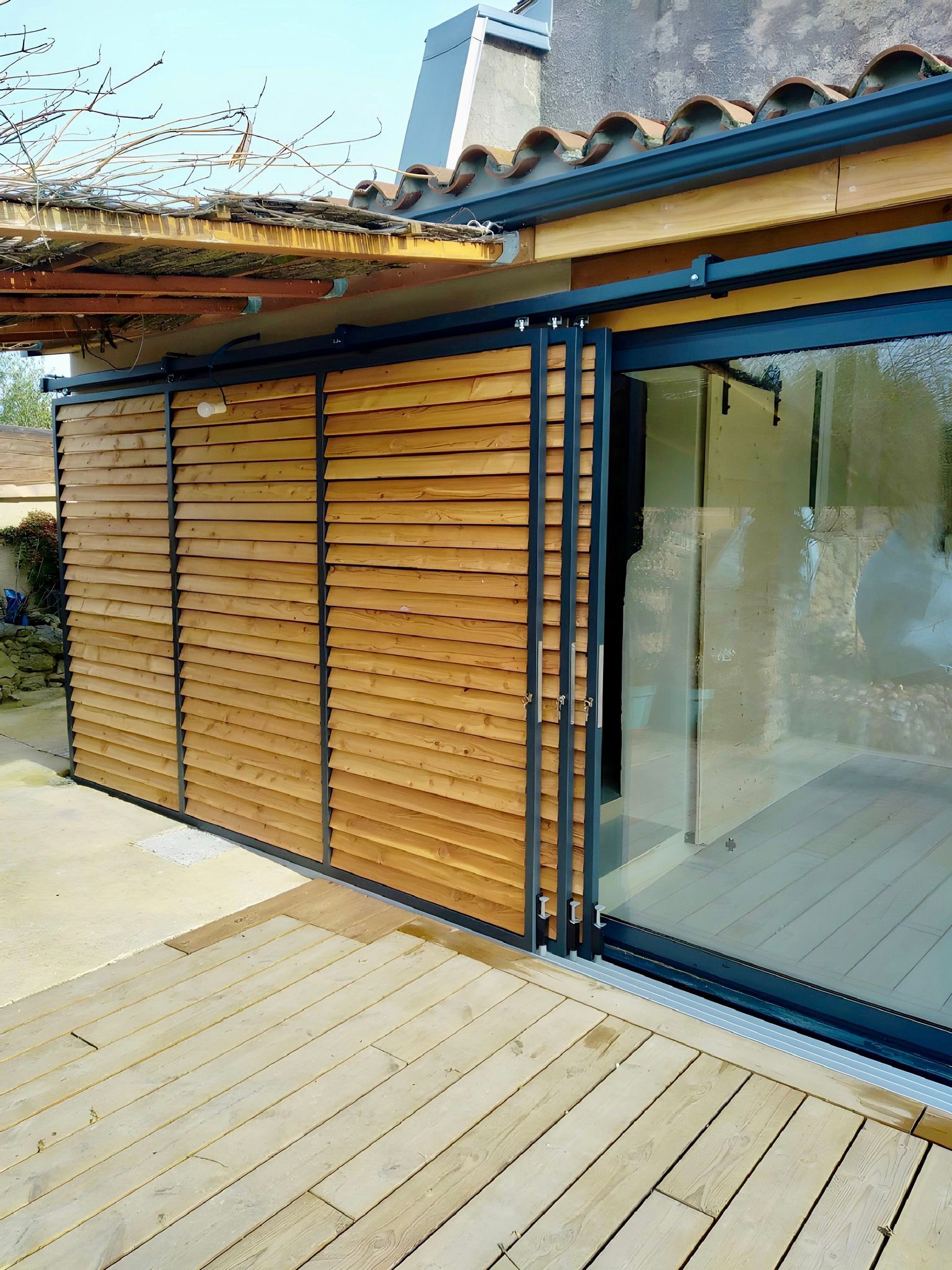 Extérieur d'un bâtiment avec bardage en bois, portes coulissantes en verre et revêtement en lattes de bois.