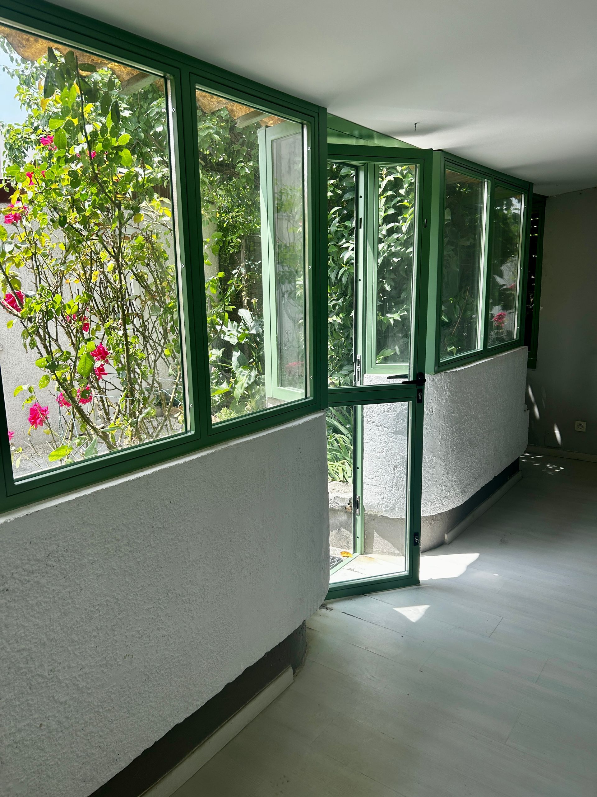 Verrière en acier verte avec porte dans véranda et vue sur jardin.