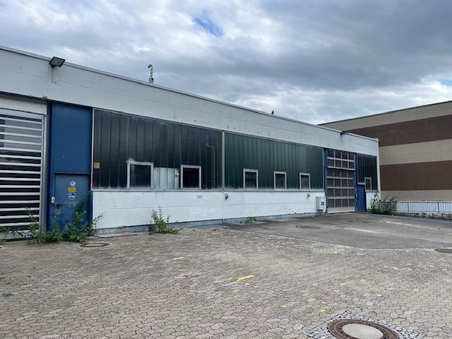 Eine große Lagerhalle mit vielen Fenstern und einer blauen Tür.