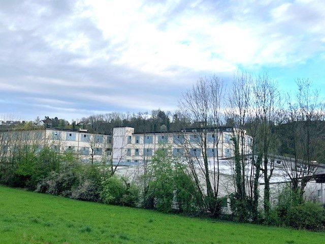 Ein großes Gebäude ist von Bäumen und Gras auf einem Feld umgeben.