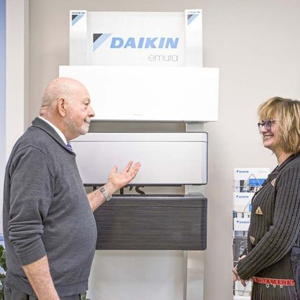 Un homme fait un geste vers l'écran d'un climatiseur Daikin et parle à une femme dans une salle d'exposition.