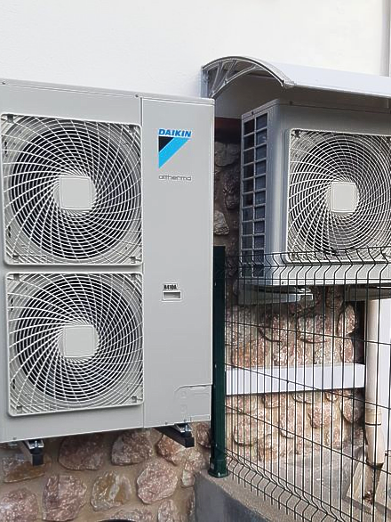 Deux unités de climatisation extérieures Daikin fixées sur un mur en pierre. L'une possède deux grilles de ventilation, l'autre une seule.