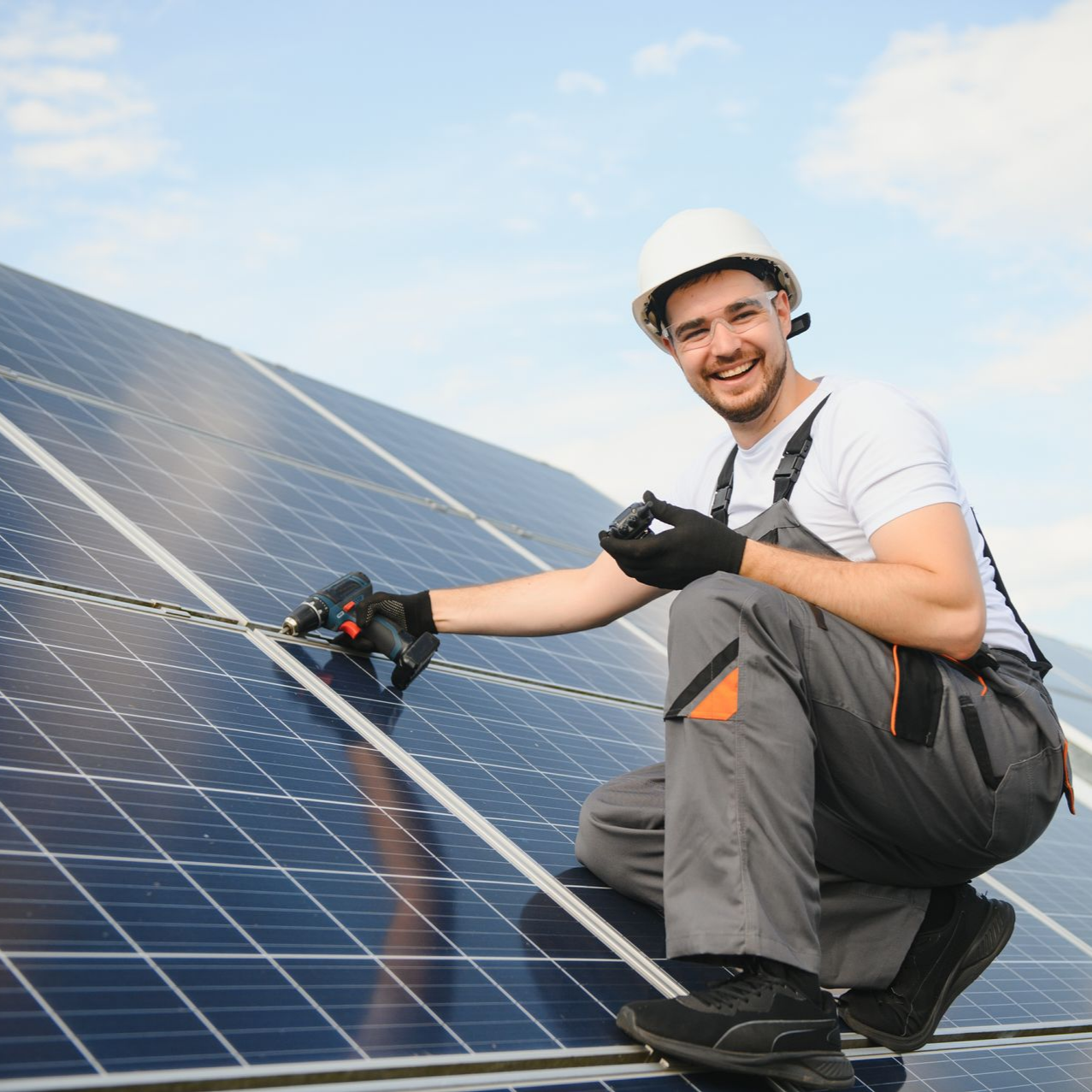 Un homme portant un casque de chantier installe des panneaux solaires sur un toit et sourit à la caméra.