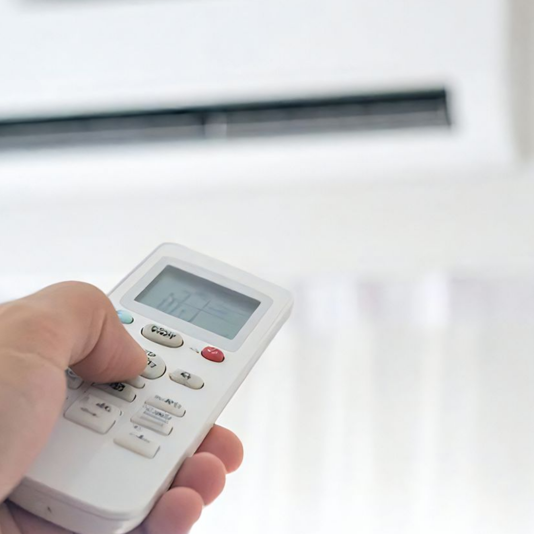 Une main tenant une télécommande blanche pointée vers un climatiseur, permettant de régler la température.
