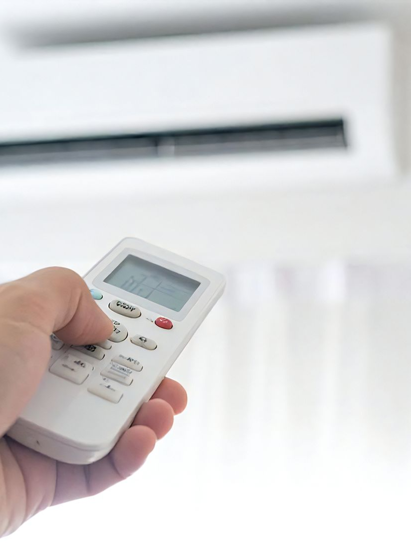 Main tenant une télécommande blanche de climatiseur, pointant vers un climatiseur blanc.