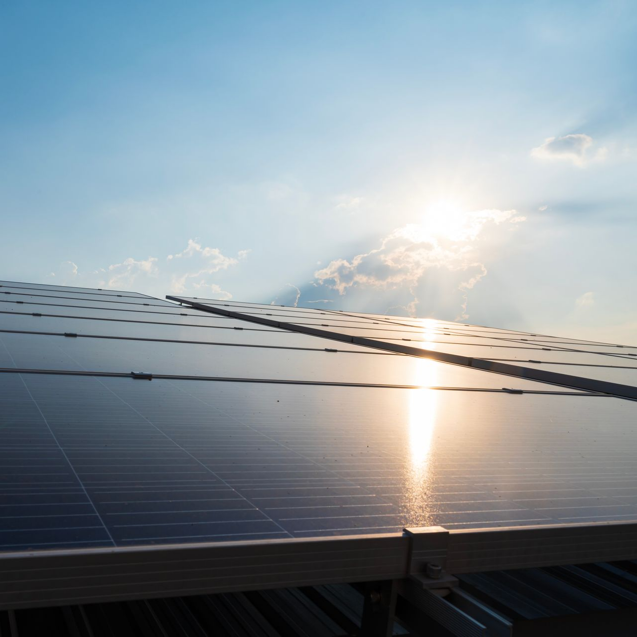 Des panneaux solaires installés sur un toit réfléchissent la lumière du soleil sur un ciel bleu partiellement nuageux.