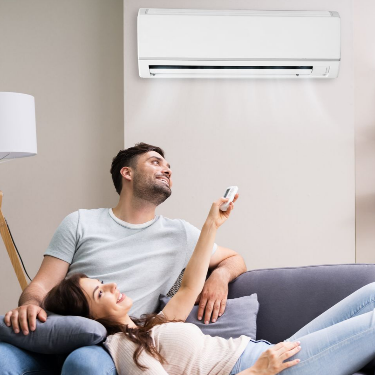 Un couple se détend sur un canapé, utilisant la télécommande du climatiseur dans le salon.