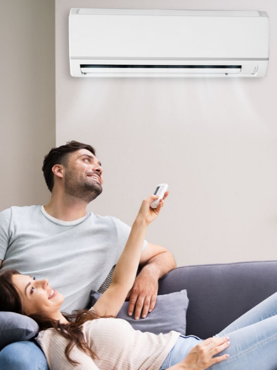 Un couple se détend sur un canapé, en actionnant un climatiseur mural à l'aide d'une télécommande.
