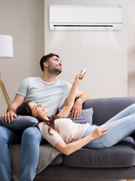 Couple se relaxant sur un canapé, femme tenant une télécommande, climatiseur au-dessus.