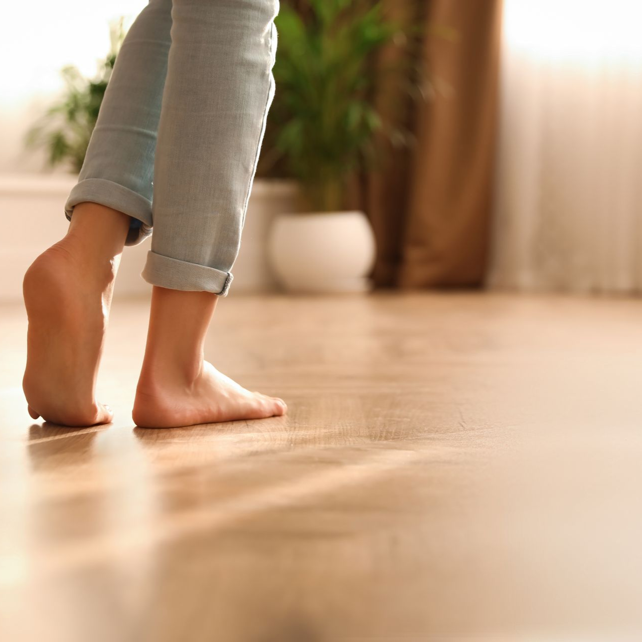 Des pieds nus marchent sur un parquet, la lumière du soleil entrant par une fenêtre.