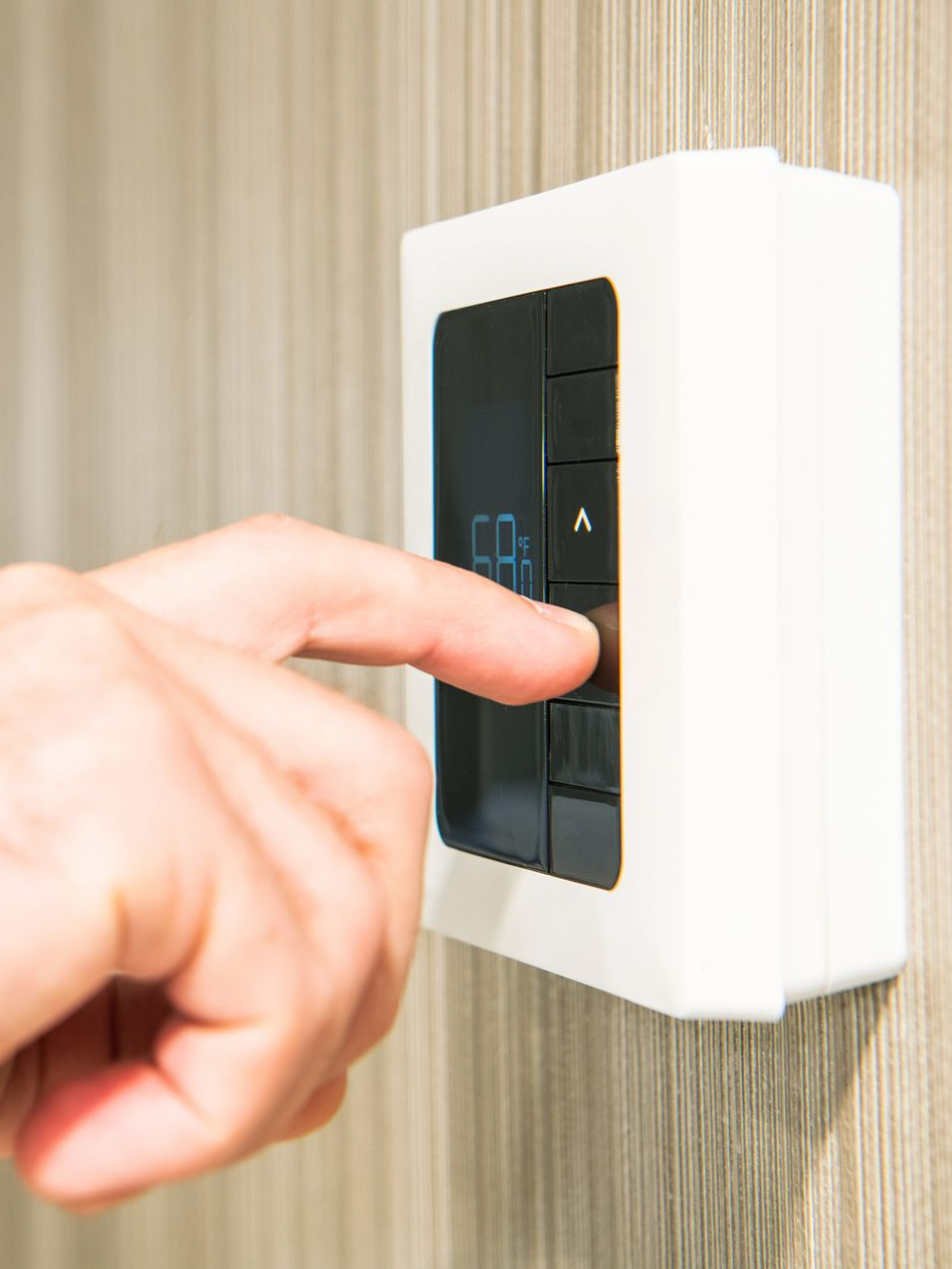 Le doigt d'une personne appuyant sur un bouton noir d'un panneau de commande mural rectangulaire blanc.