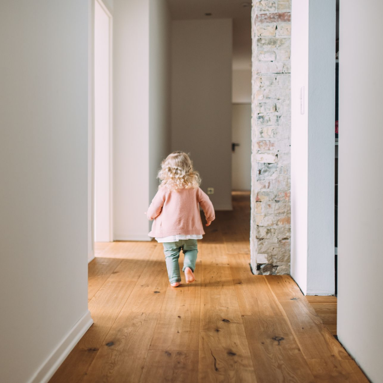 Un enfant s'éloigne dans un couloir au sol en bois.