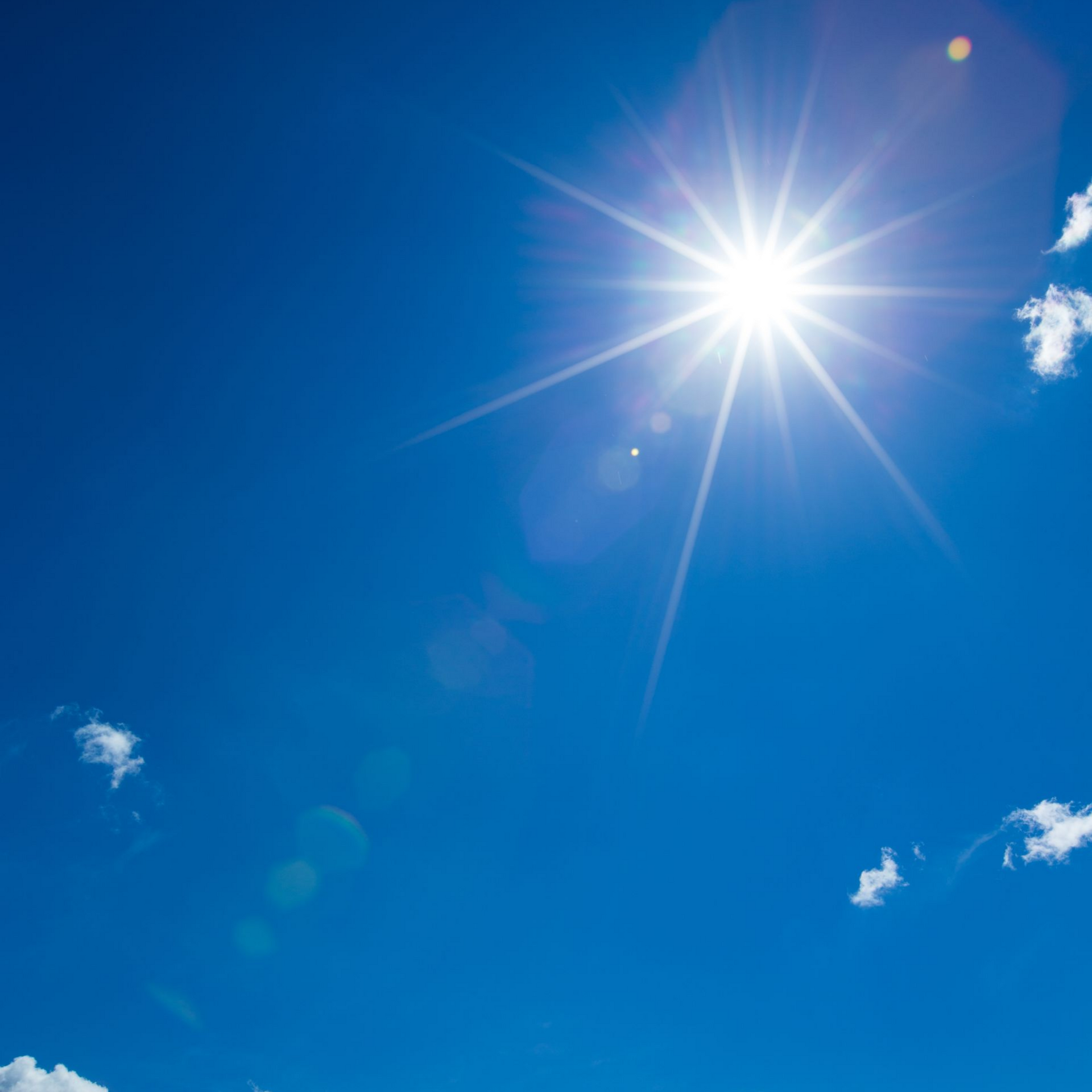 Un soleil éclatant brille dans un ciel d'un bleu vibrant parsemé de quelques petits nuages ​​blancs.