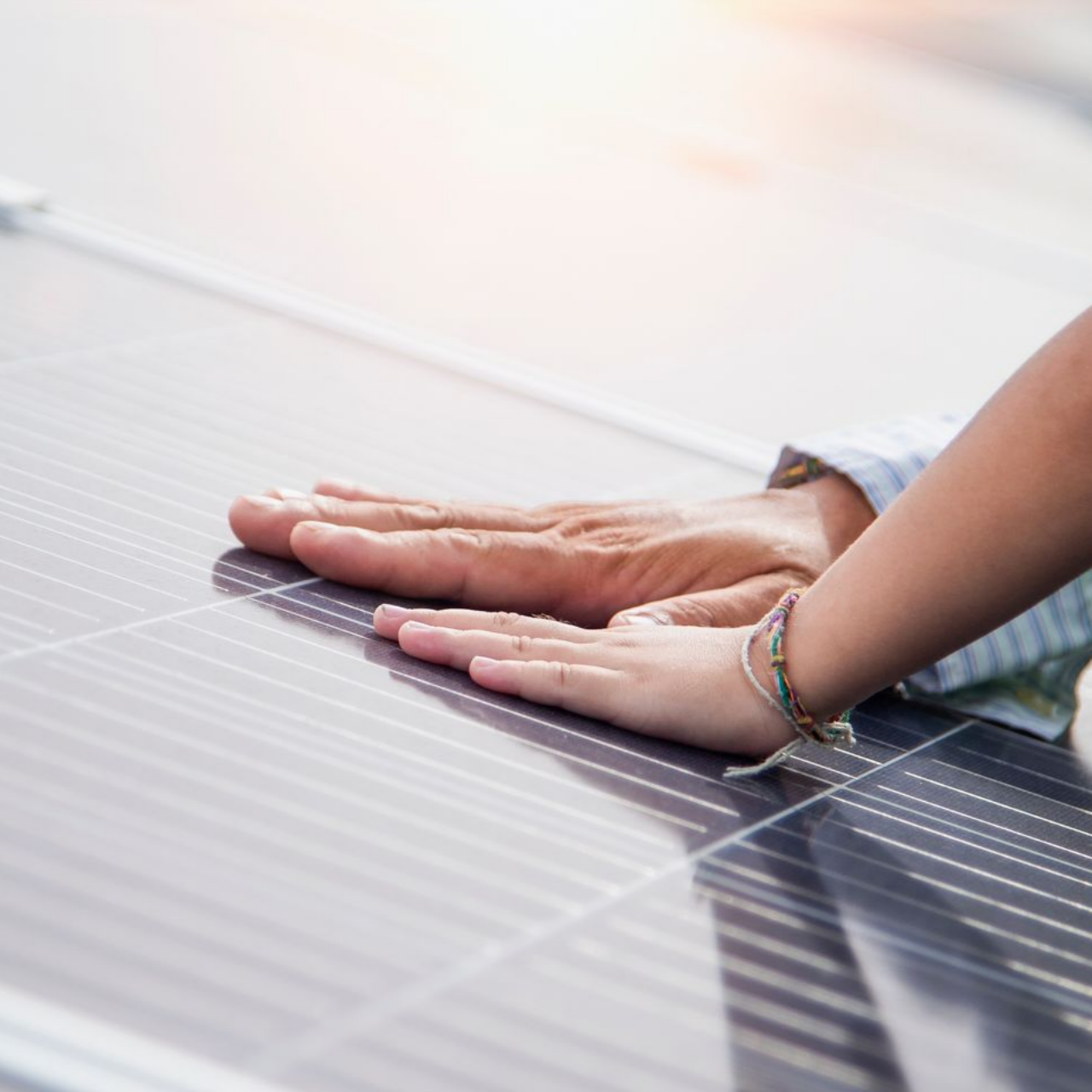 Les mains d'un adulte et d'un enfant touchant un panneau solaire, avec le soleil en arrière-plan.