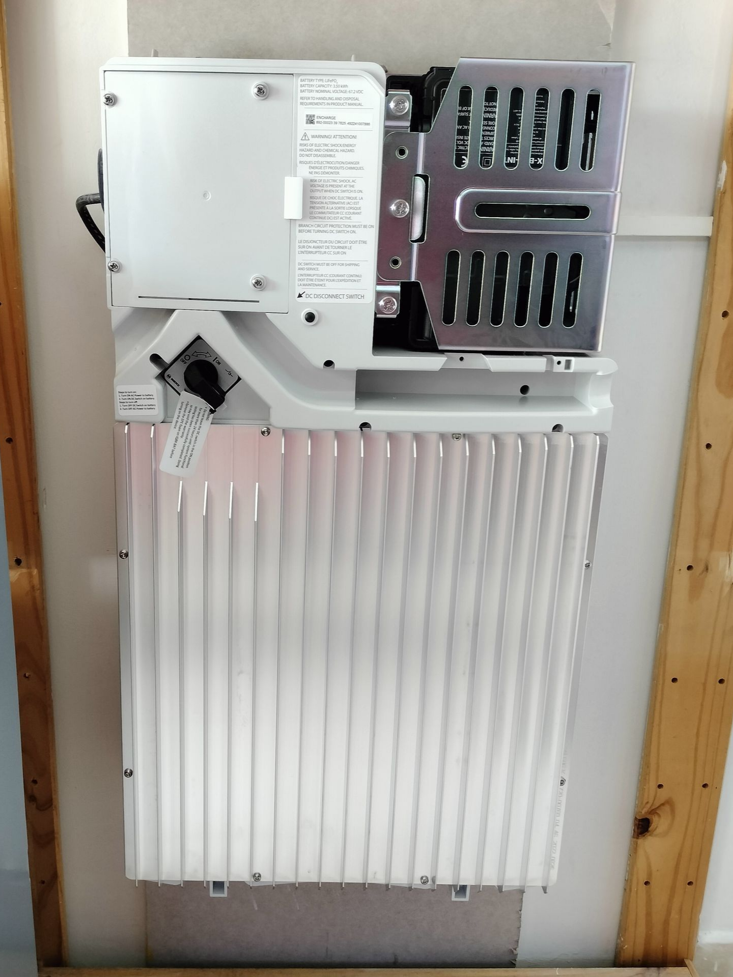 Onduleur solaire blanc monté sur un cadre en bois, avec un panneau de ventilation métallique et un extérieur nervuré.