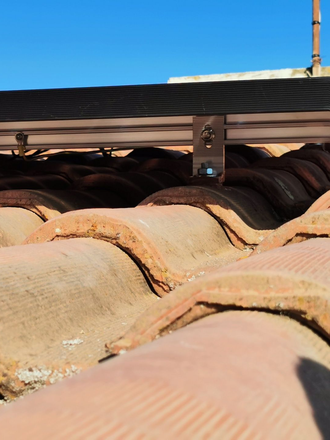 Tuiles de toit en terre cuite avec matériel de fixation pour panneaux solaires, sur fond de ciel bleu.
