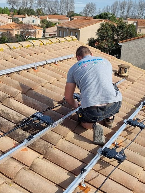 Un homme portant un t-shirt Daikin installe des panneaux solaires sur un toit en tuiles.