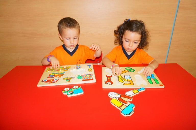 Un niño y una niña están jugando con rompecabezas en una mesa roja.